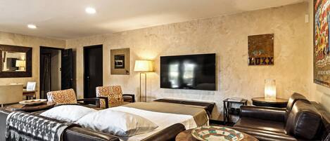 A hotel room with a bed, a sofa, a TV, a lamp, and a painting on the wall.