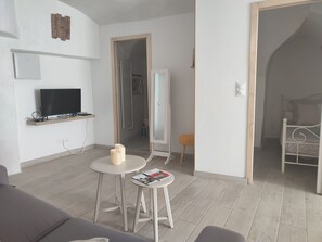 Una sala moderna con televisor de pantalla plana, una mesita redonda con revistas, un sofá y una cama en la habitación contigua.
