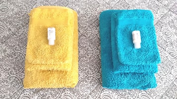 Two folded towels, one yellow and one blue, with a bottle of hand sanitizer placed on top of each.
