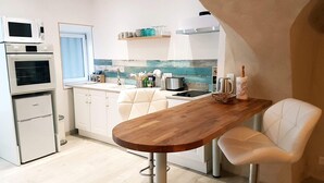 A compact kitchen with a wooden dining table, white chairs, and built-in appliances including a microwave and oven. - Les insolites de Champeix (Champeix)