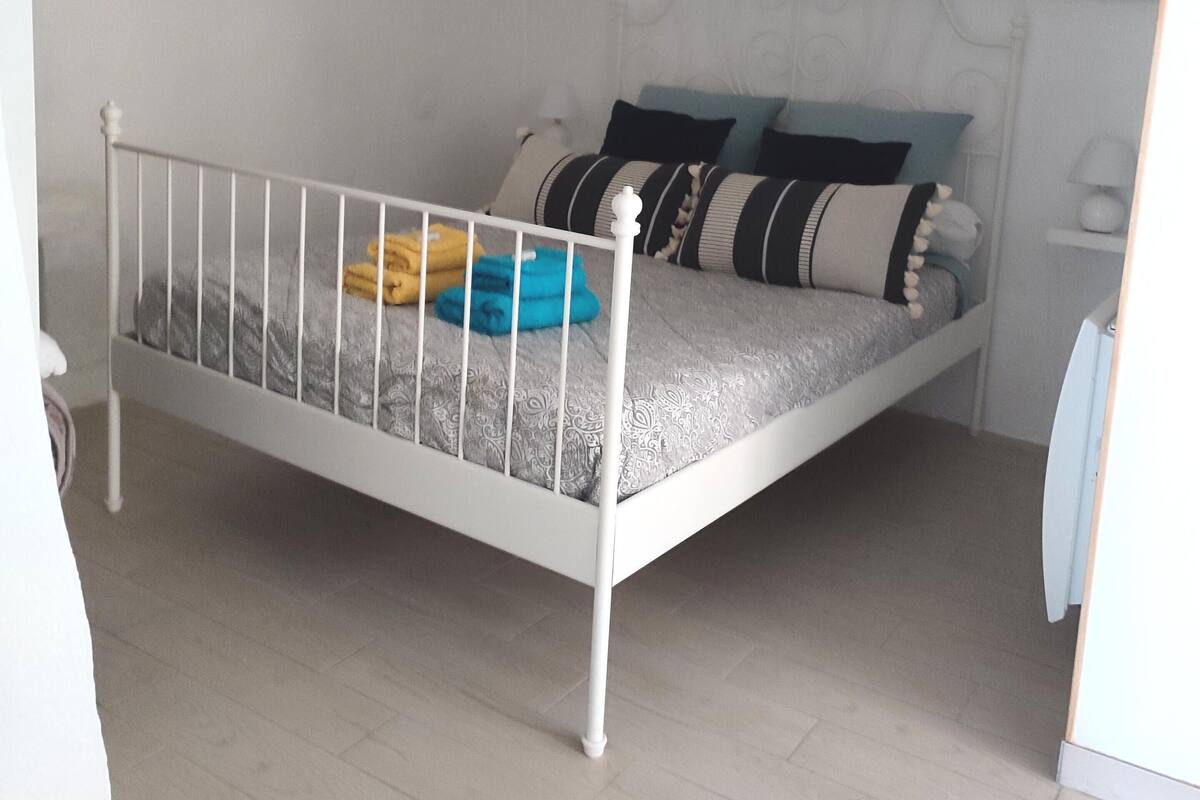 A single bed with a metal frame, a bedside table with a lamp, and a ceiling light fixture.