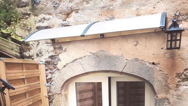 A small, enclosed patio area with a sliding glass door, a wooden gate, and a stone wall. - Les insolites de Champeix (Champeix)