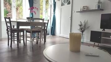 A dining area with a round table, chairs, and a candle. There is a television on a stand and a door with a window.