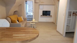 A modern living room with a wooden dining table, a sofa with yellow cushions, a small round table with candles, and a TV mounted on the wall. - Les insolites de Champeix (Champeix)
