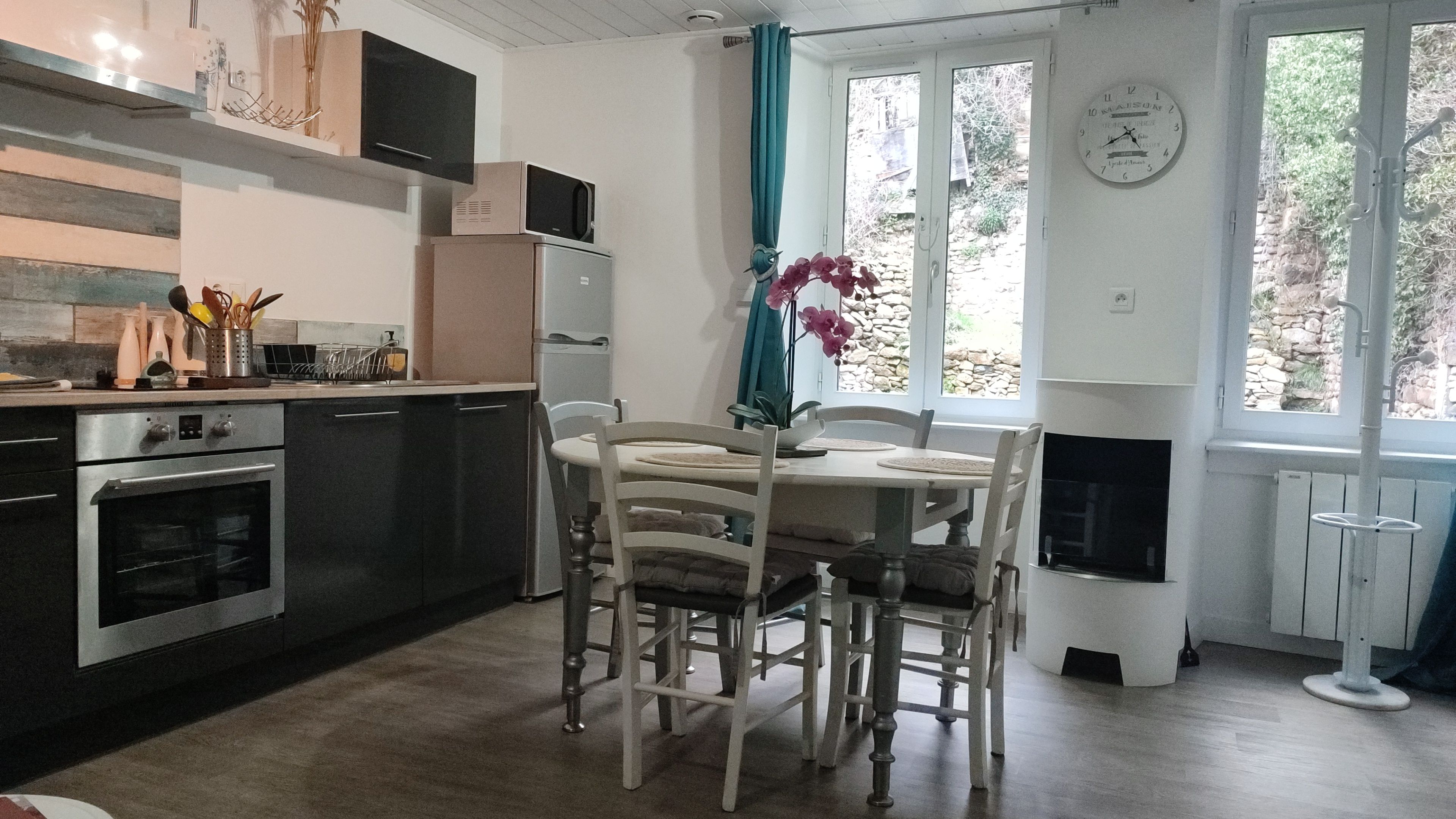 A kitchen with a dining table, chairs, and a clock on the wall.
