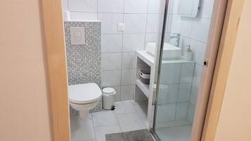 Pieni, moderni kylpyhuone, jossa on wc, pesuallas ja suihku.