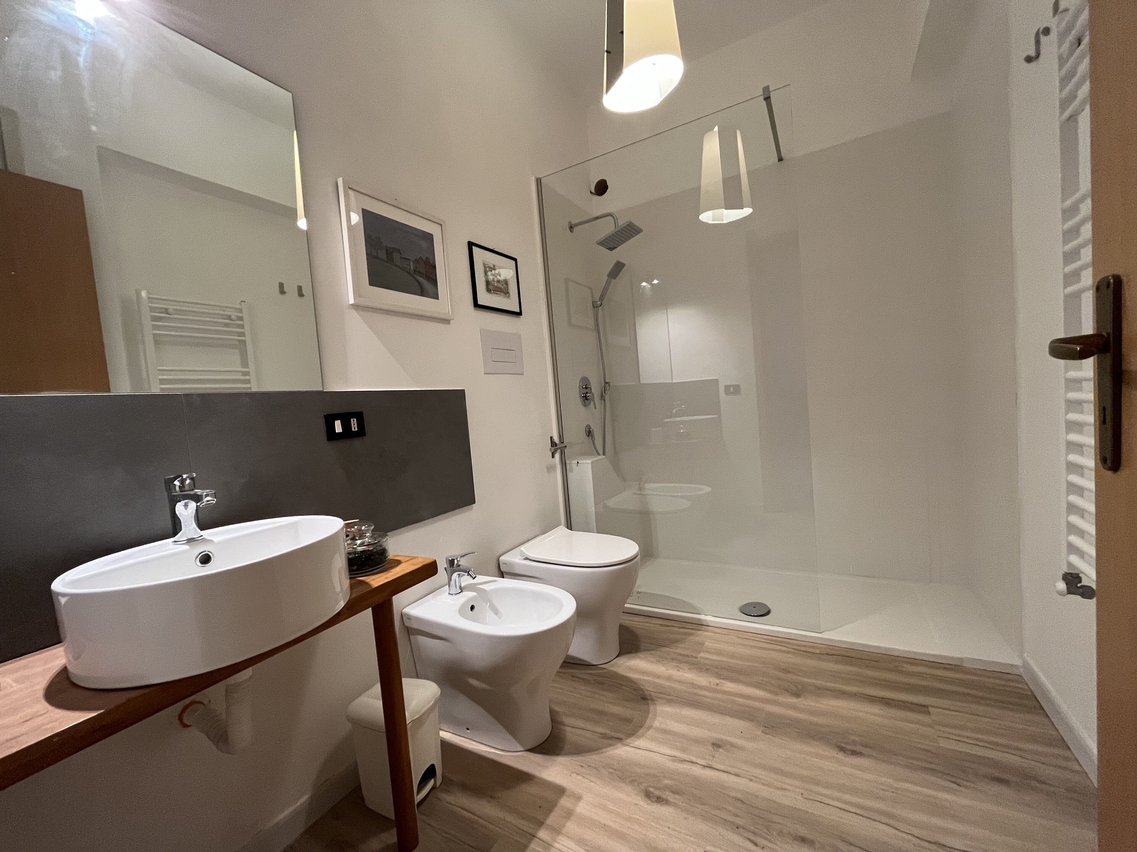 Un baño moderno con un espejo grande, un lavabo, un bidé y una ducha con mampara de vidrio.