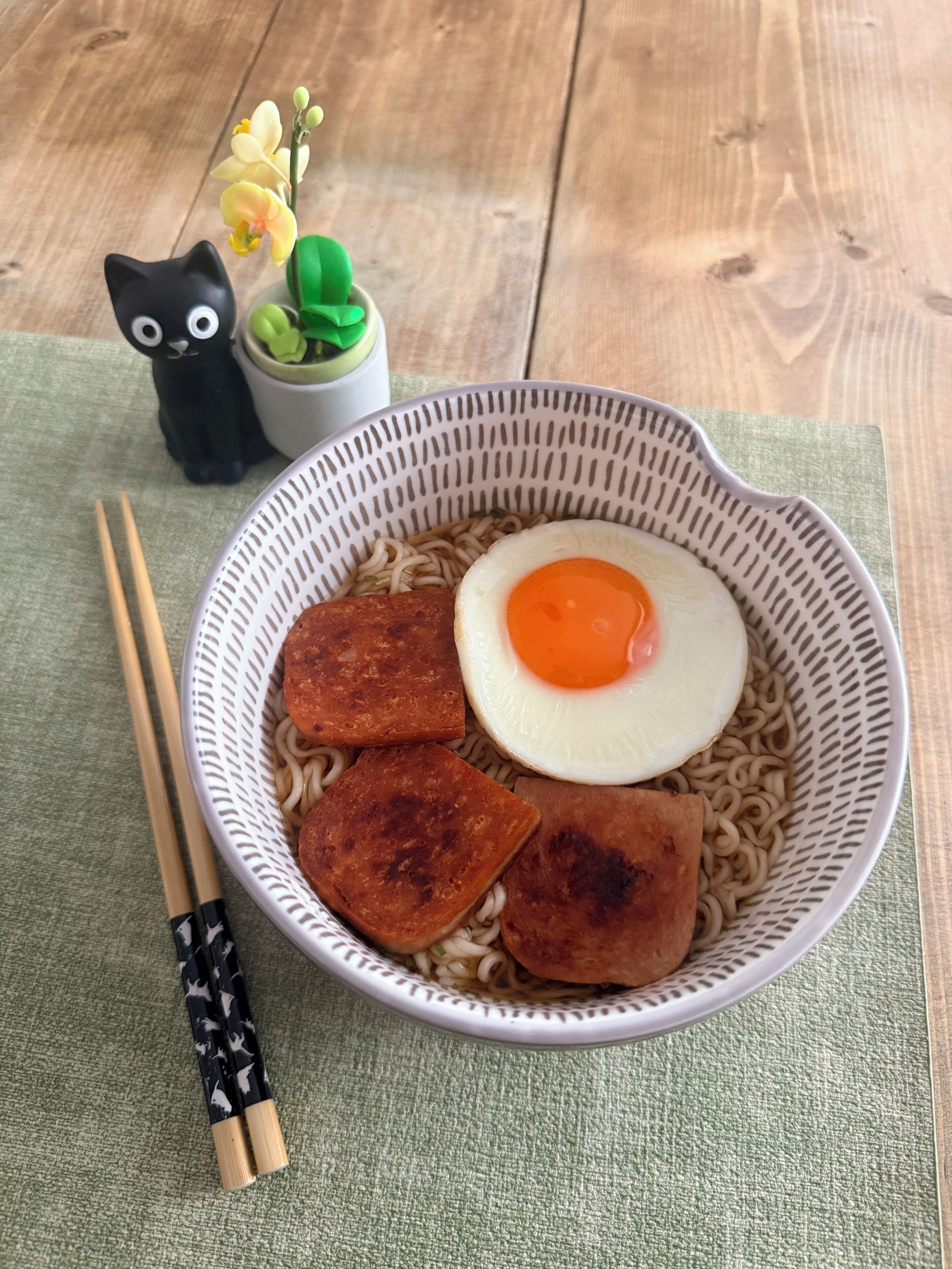 Eine Schüssel Ramen mit Spiegelei und Tofustückchen auf einer gewebten Matte.