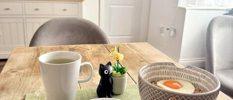 A dining table with a cup of tea, a plate with food, chopsticks, a small black cat figurine, and a potted plant.