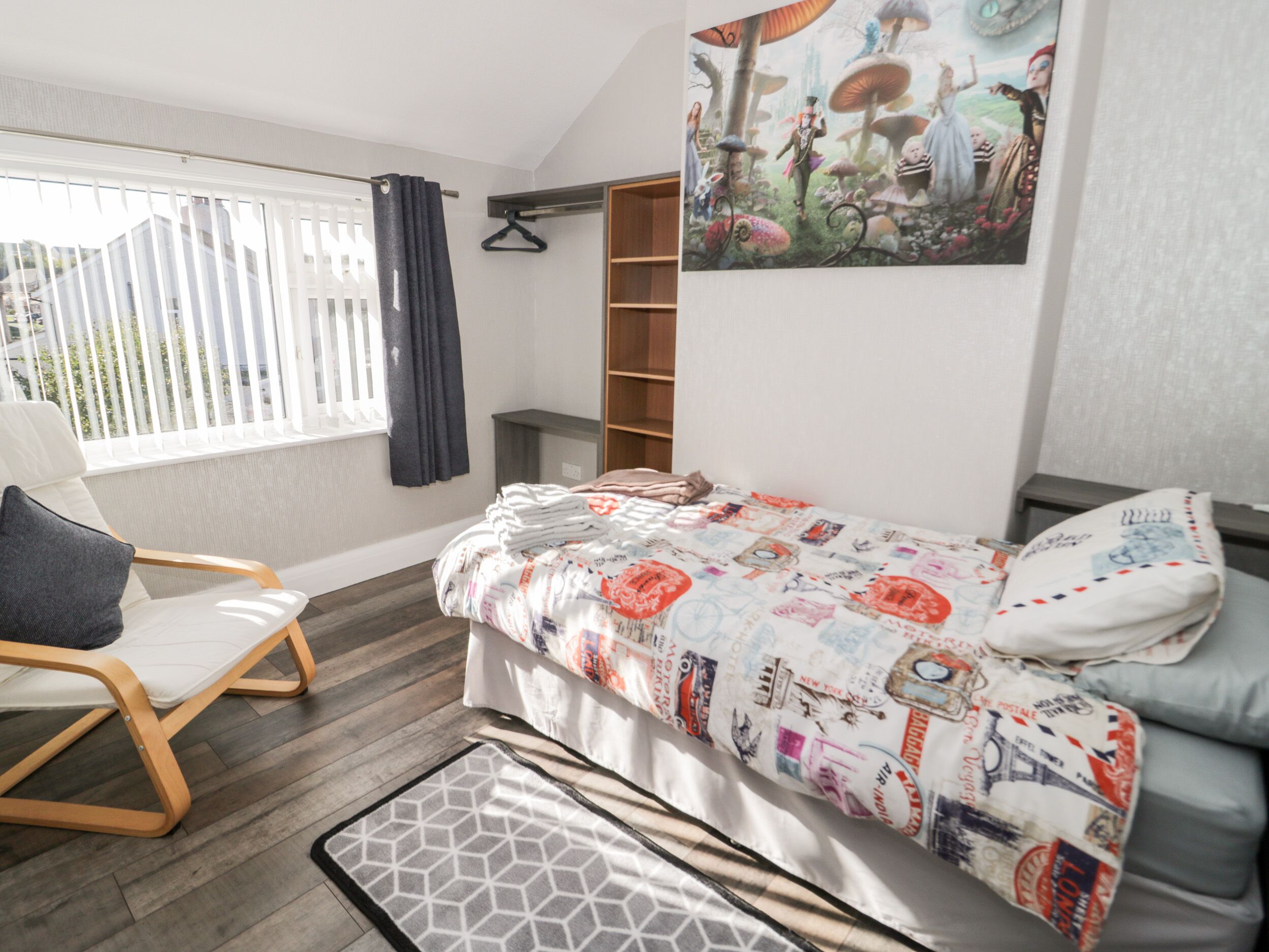 Un dormitorio moderno con una cama, una silla, una ventana con cortinas, un estante en la pared y un cartel.