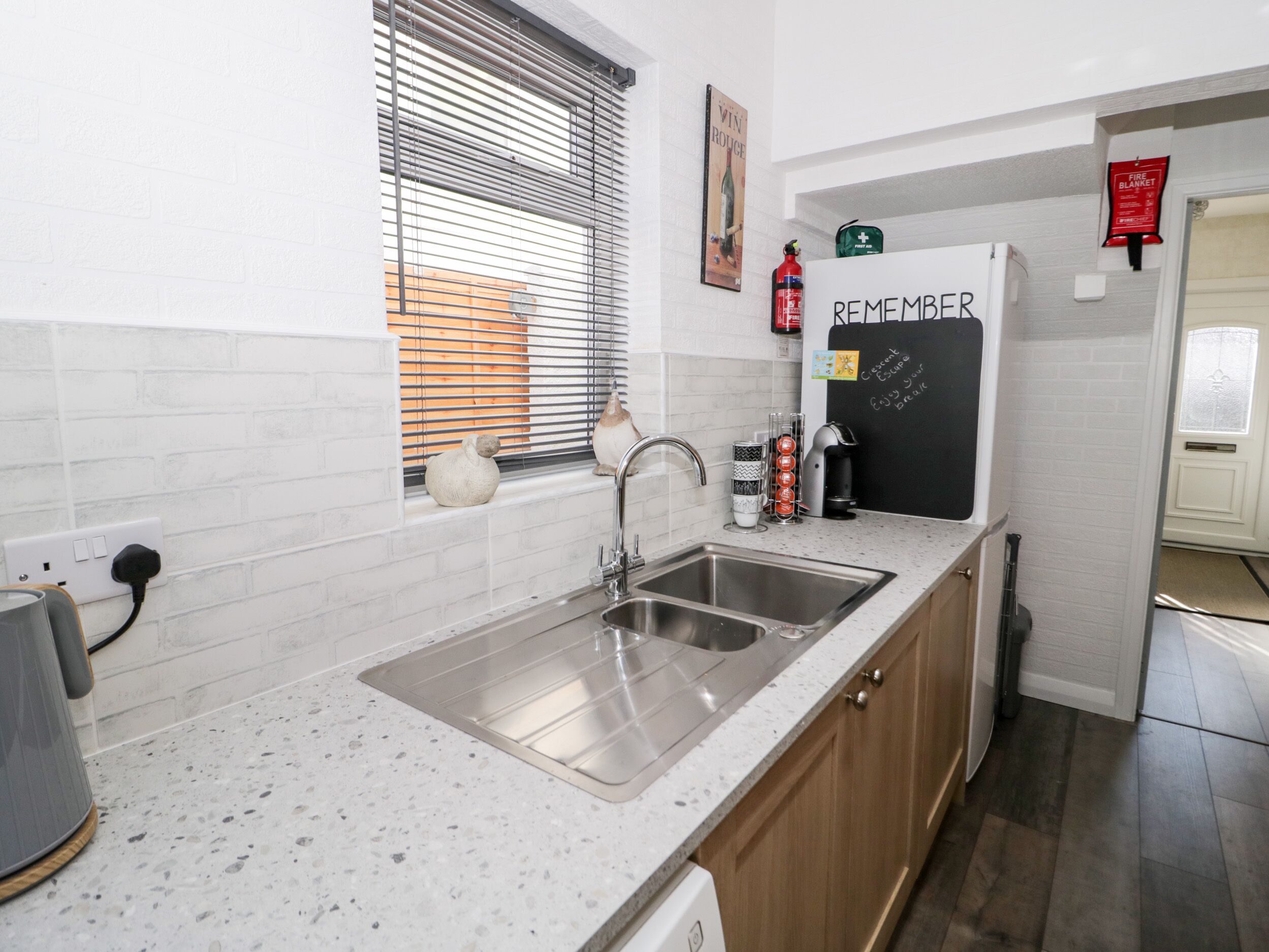A modern kitchen with a stainless steel sink, wooden cabinets, and a chalkboard with the word "REMEMBER" written on it.