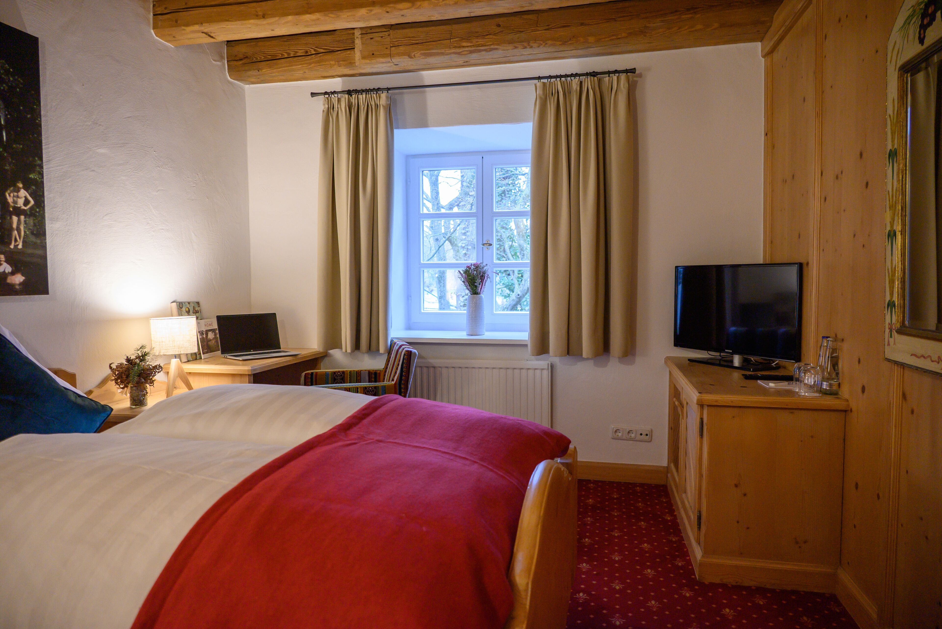 Ein Hotelzimmer mit Bett, Schreibtisch, Laptop, Fernseher und einem Fenster mit Vorhängen.