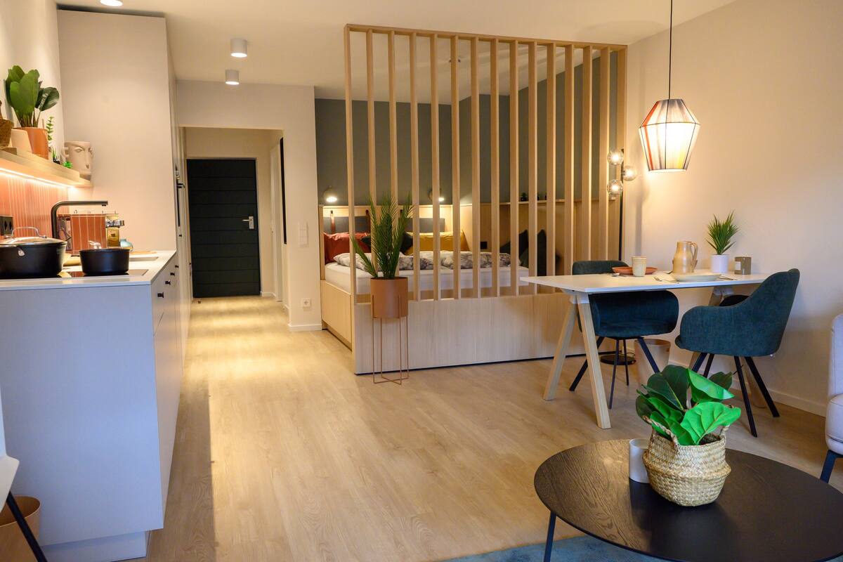 A modern kitchen with a dining area, wooden partition, and a hanging light fixture.