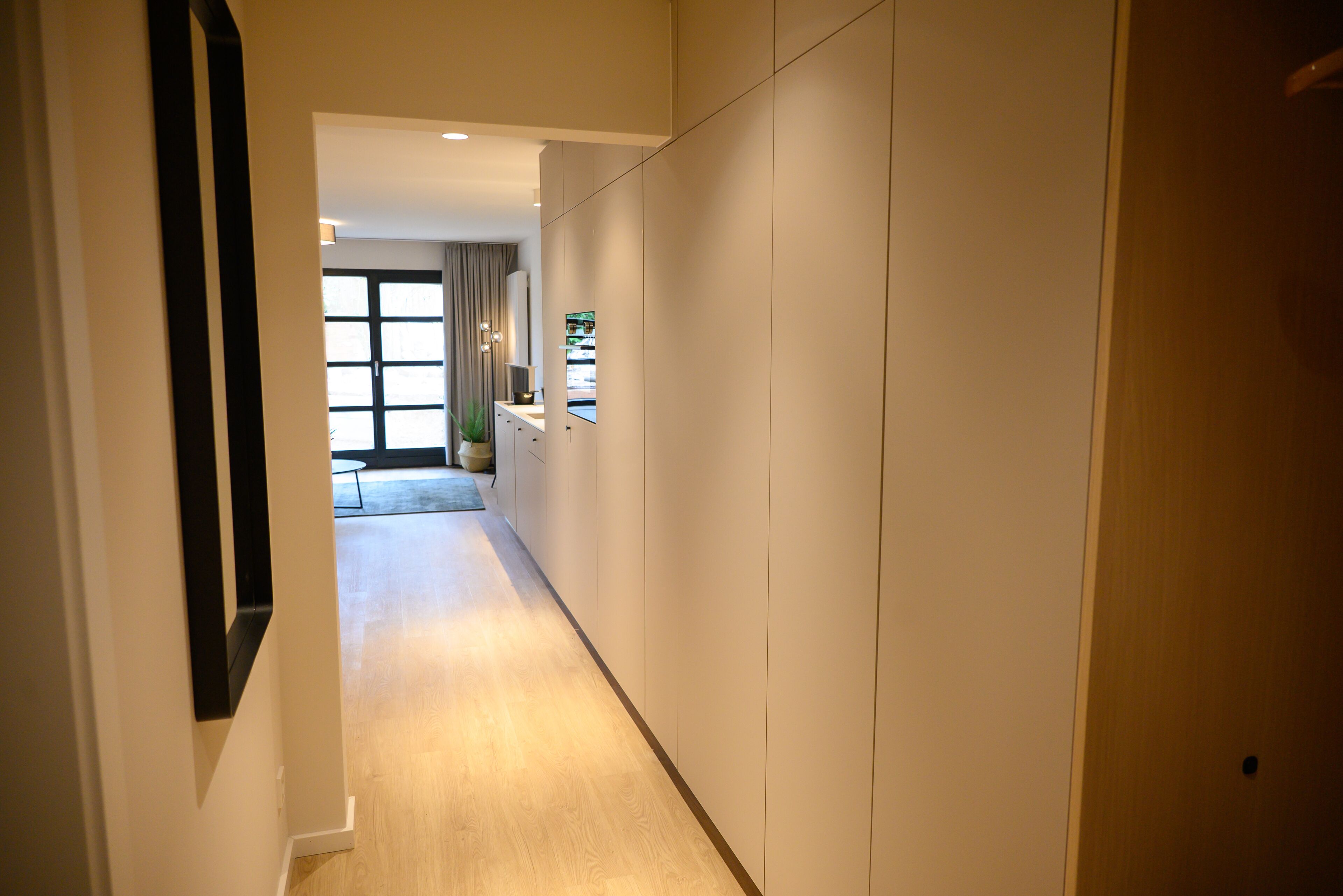 A hallway with a wooden floor, white walls, and a door on the right.