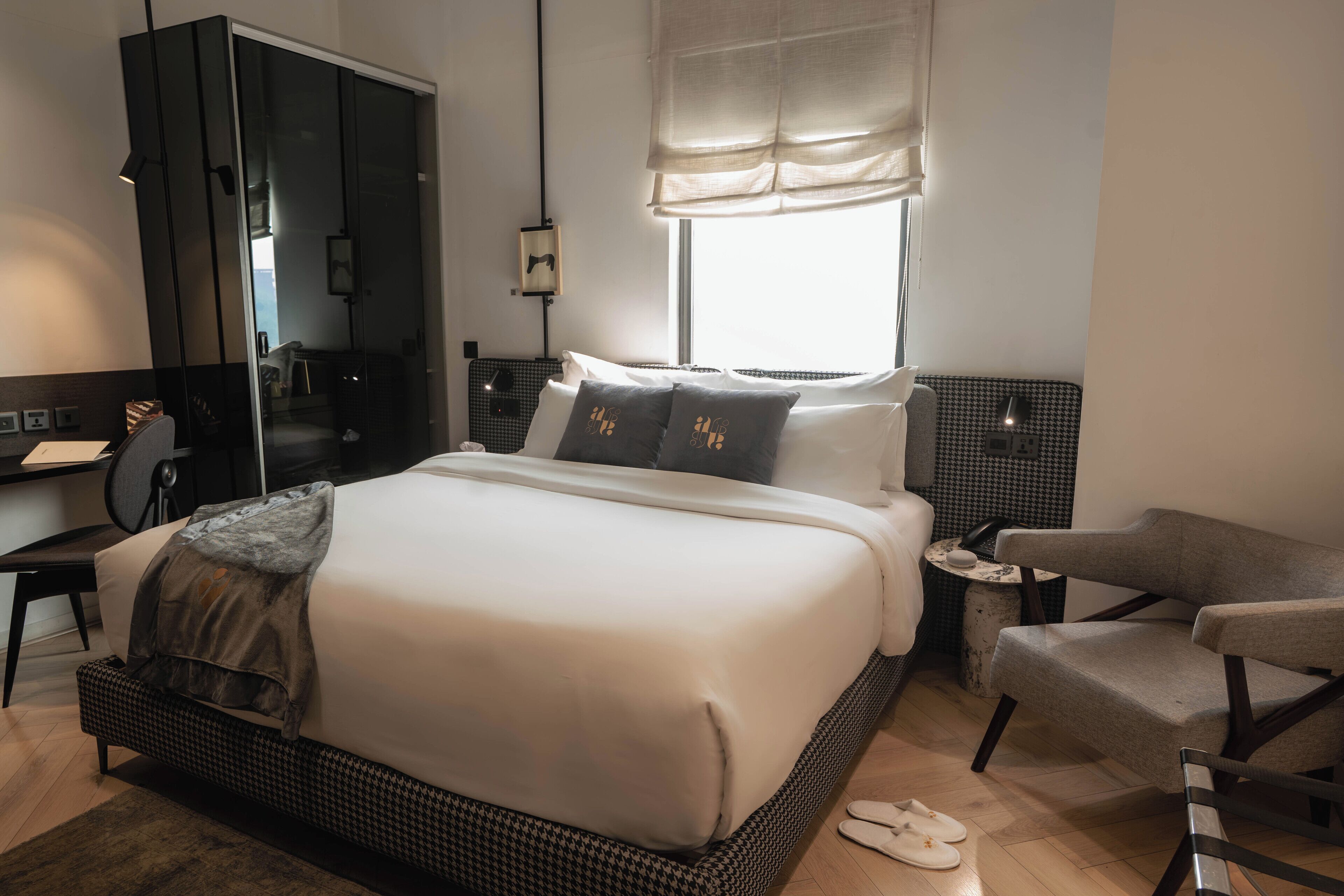 Ein modernes Hotelzimmer mit einem großen Bett, einer Sitzecke mit einem Sessel, einem kleinen Tisch und einem Kleiderschrank.