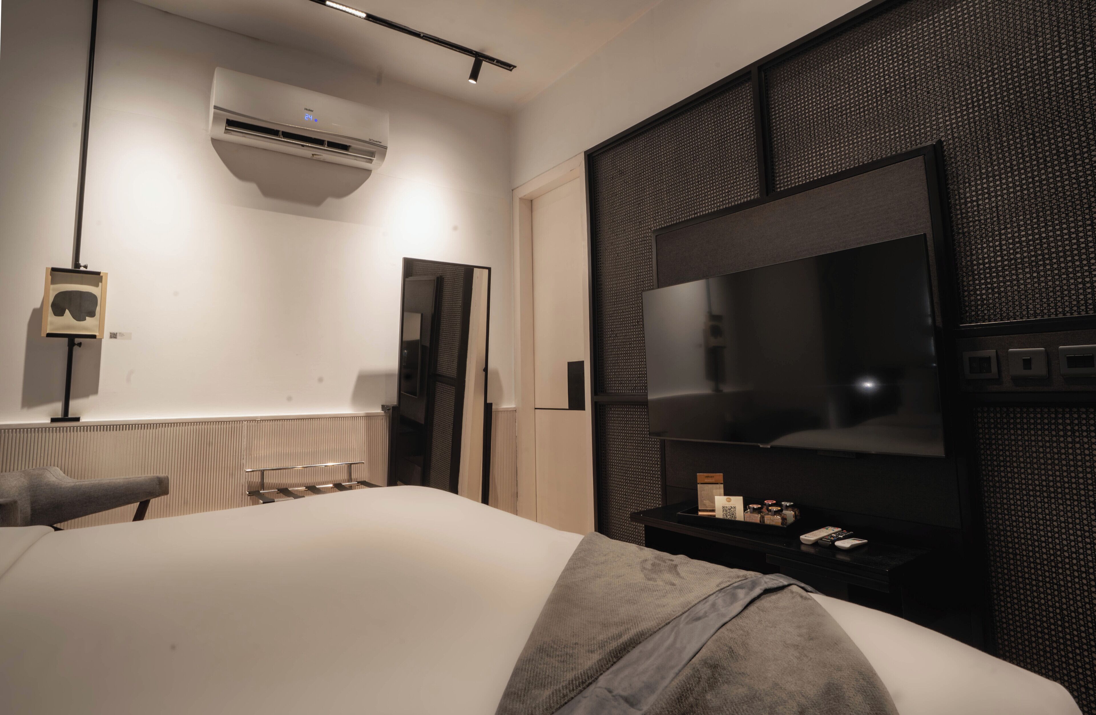 A modern hotel room with a large bed, a flat-screen TV, a wall-mounted air conditioner, and a large mirror.