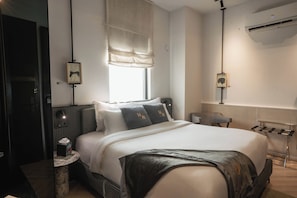 Habitació d'hotel moderna amb un llit gran, una taula de nit, una cadira i una finestra amb cortines.