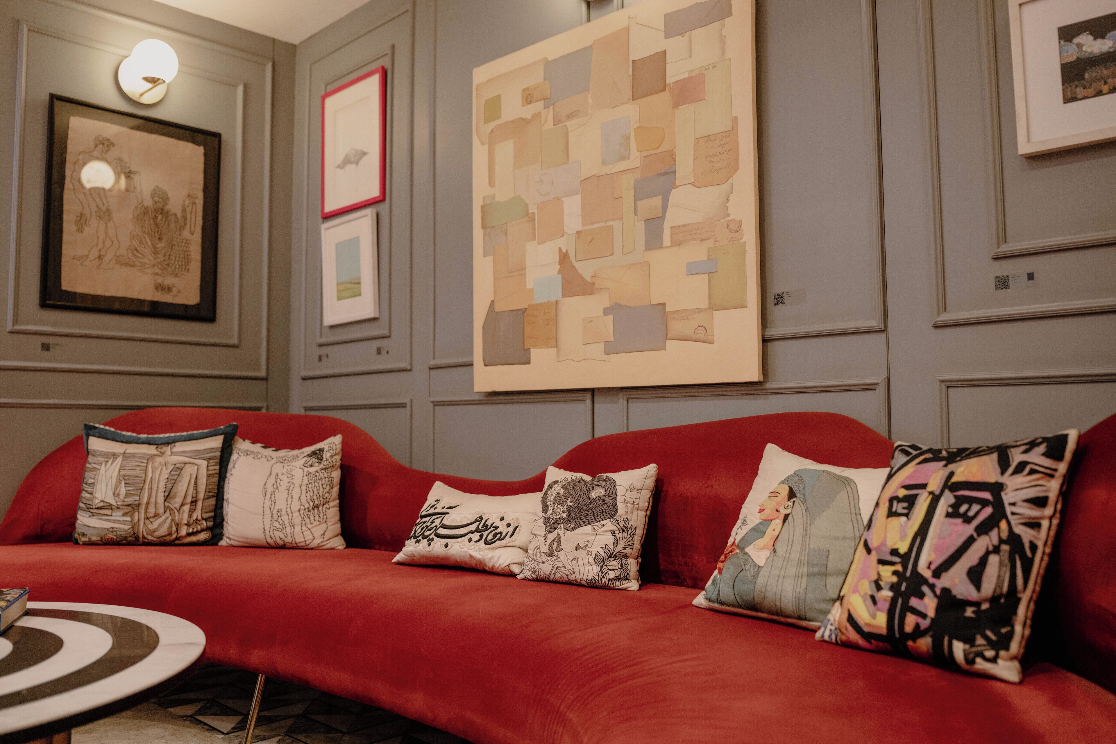A red sofa with multiple cushions, a framed artwork on the wall, and a round table with a geometric pattern.