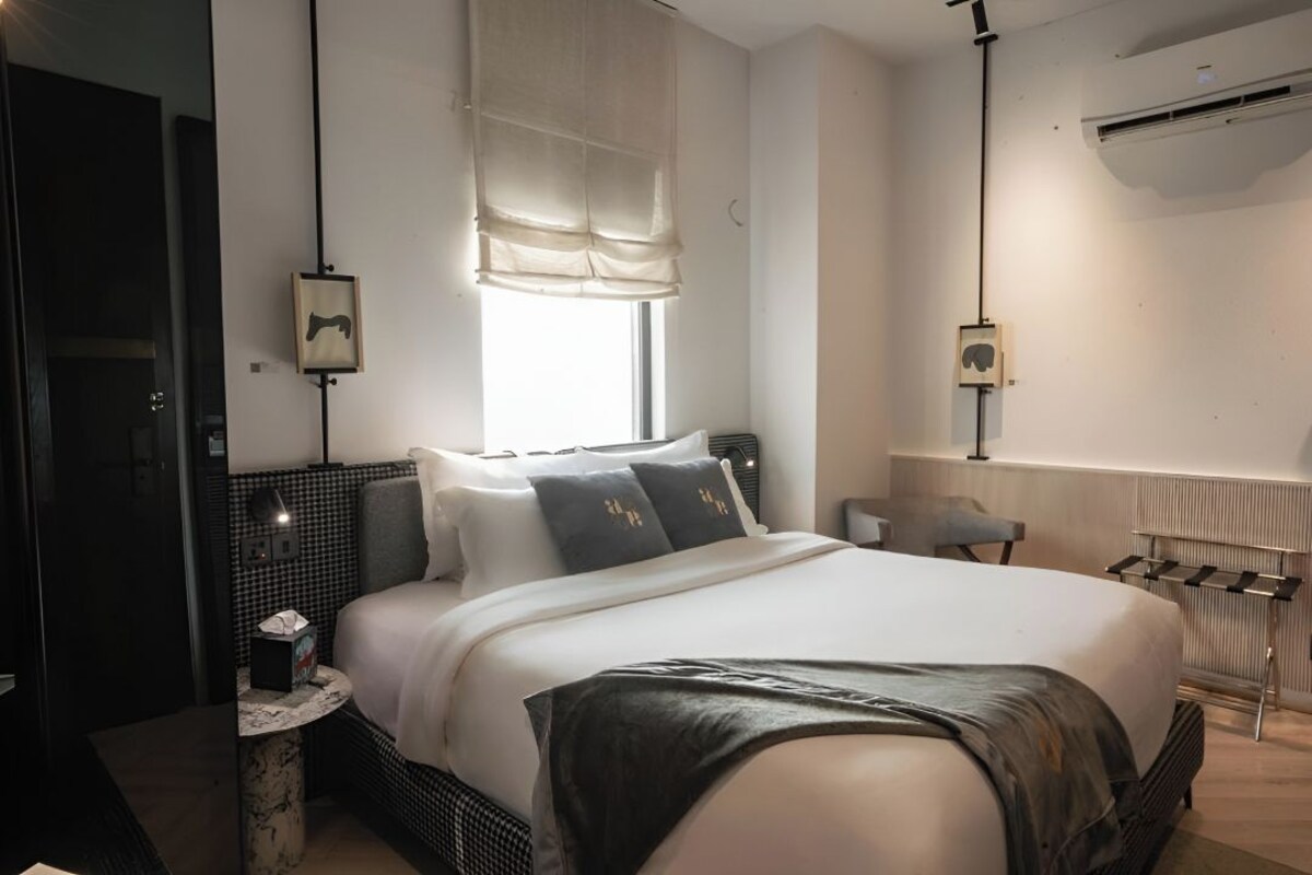 Una habitación de hotel moderna con una cama grande, mesitas de noche, un escritorio pequeño y una ventana con cortinas.