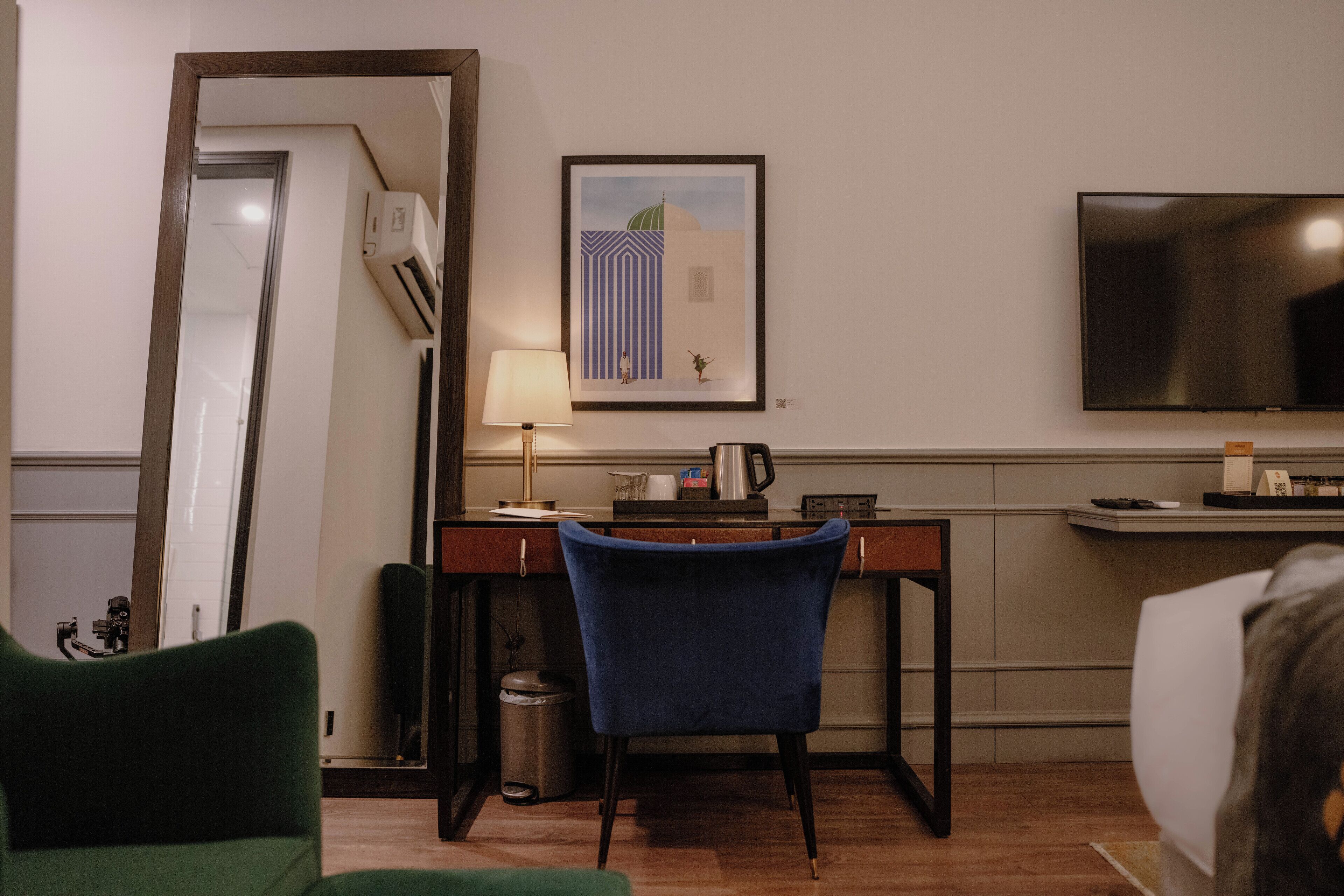Quarto de hotel com escrivaninha, cadeira, televisão e obra de arte na parede.