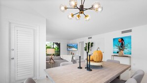 A modern dining area with a wooden table, grey upholstered chairs, a decorative pumpkin centerpiece, and a contemporary chandelier.
