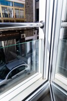 Primer plano de una puerta de vidrio con un picaporte metálico que refleja un coche y la fachada de un edificio.