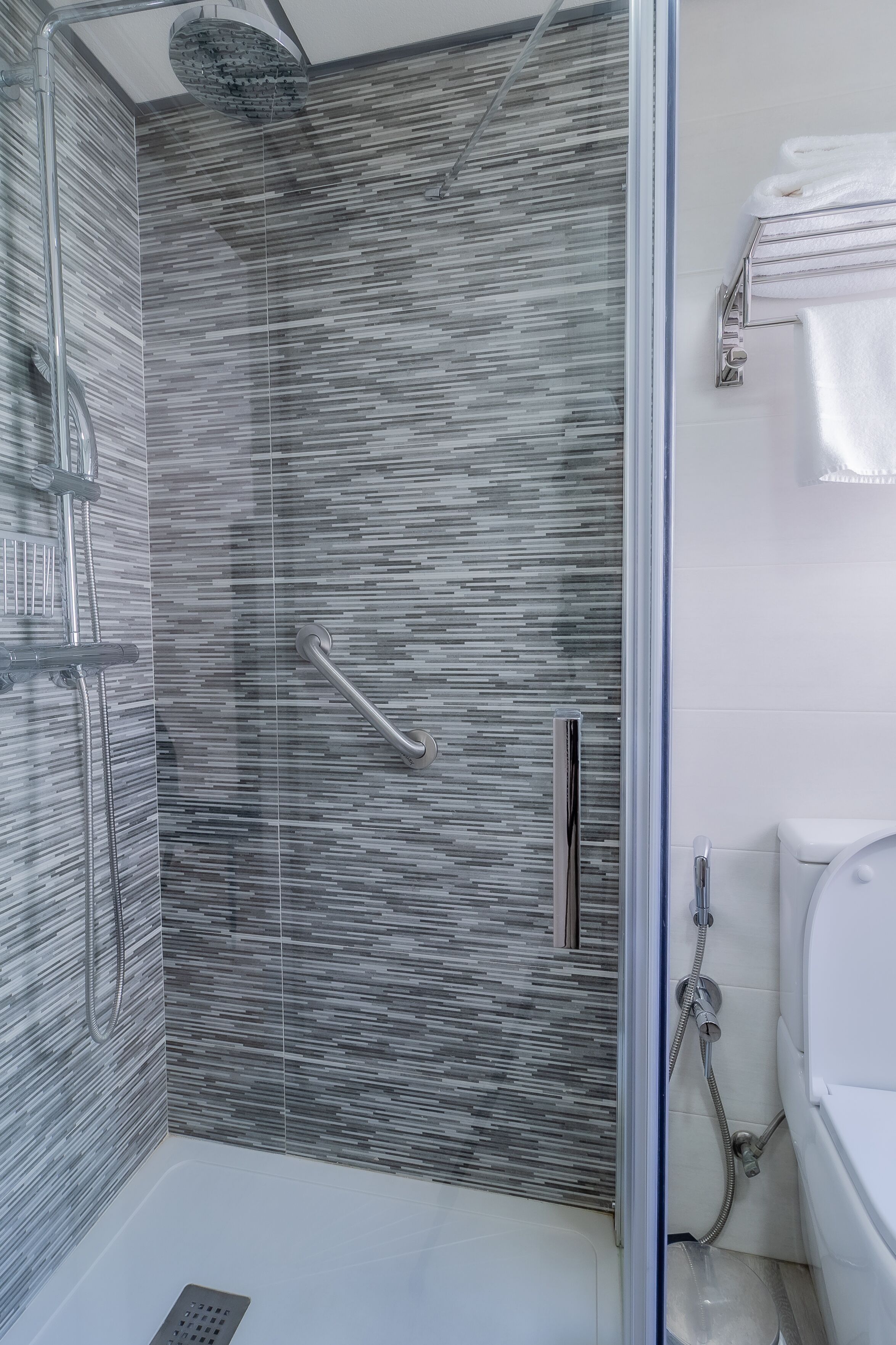 A modern bathroom with a glass shower enclosure, a white bathtub, and a towel rack.