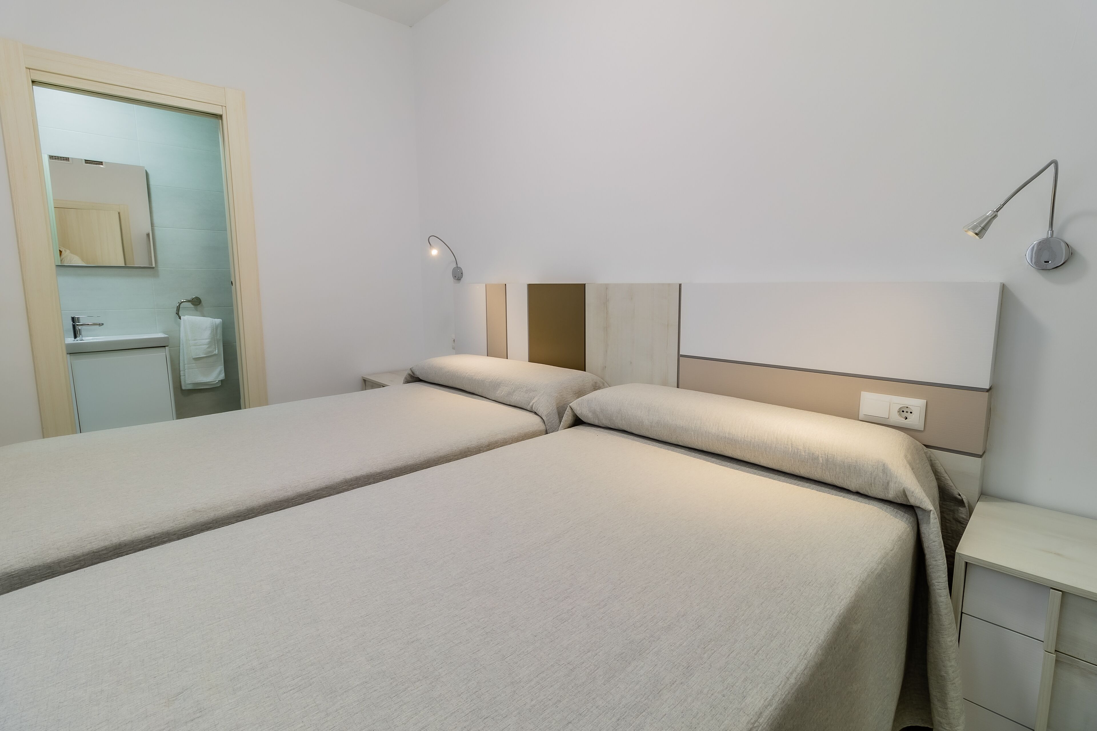 Habitación de hotel con dos camas, baño con lavamanos y dos lámparas fijadas a la pared.