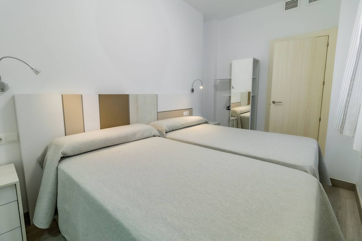 Een hotelkamer met twee enkele bedden, een nachtkastje, een lamp, een spiegel en een kledingkast.