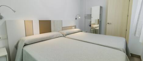 A hotel room with two single beds, a bedside table, a lamp, a mirror, and a wardrobe.