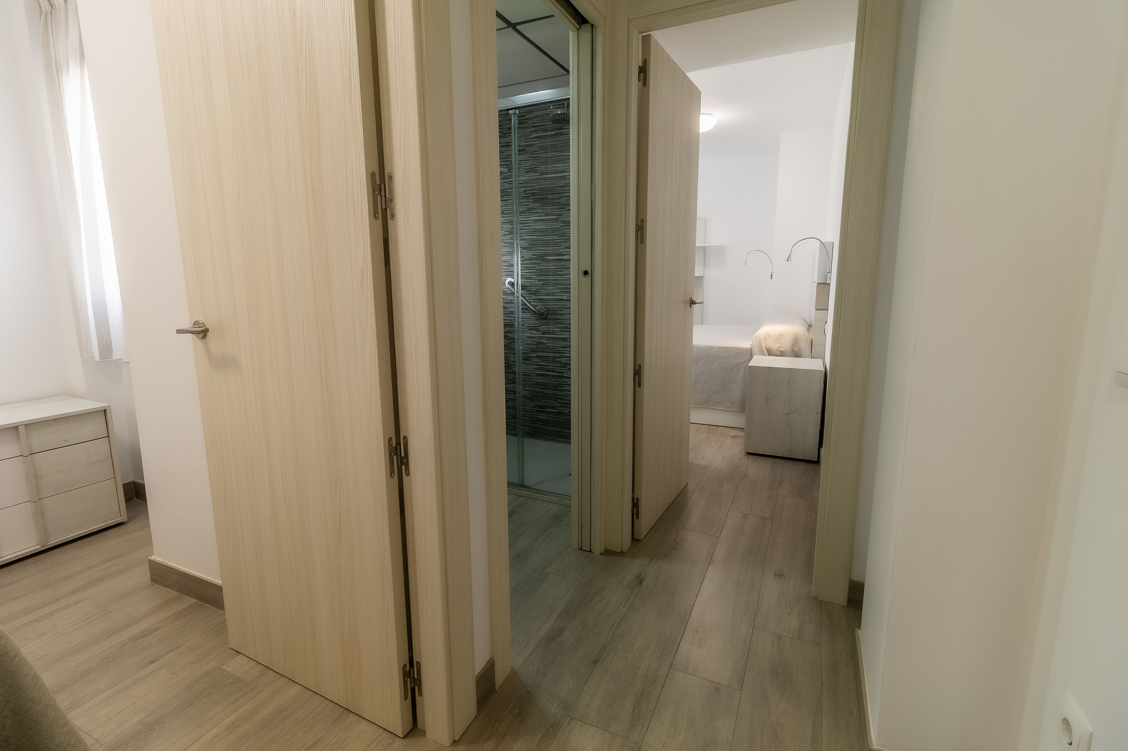 Un couloir mène à une salle de bain dotée d’une douche à parois de verre et d’une baignoire.