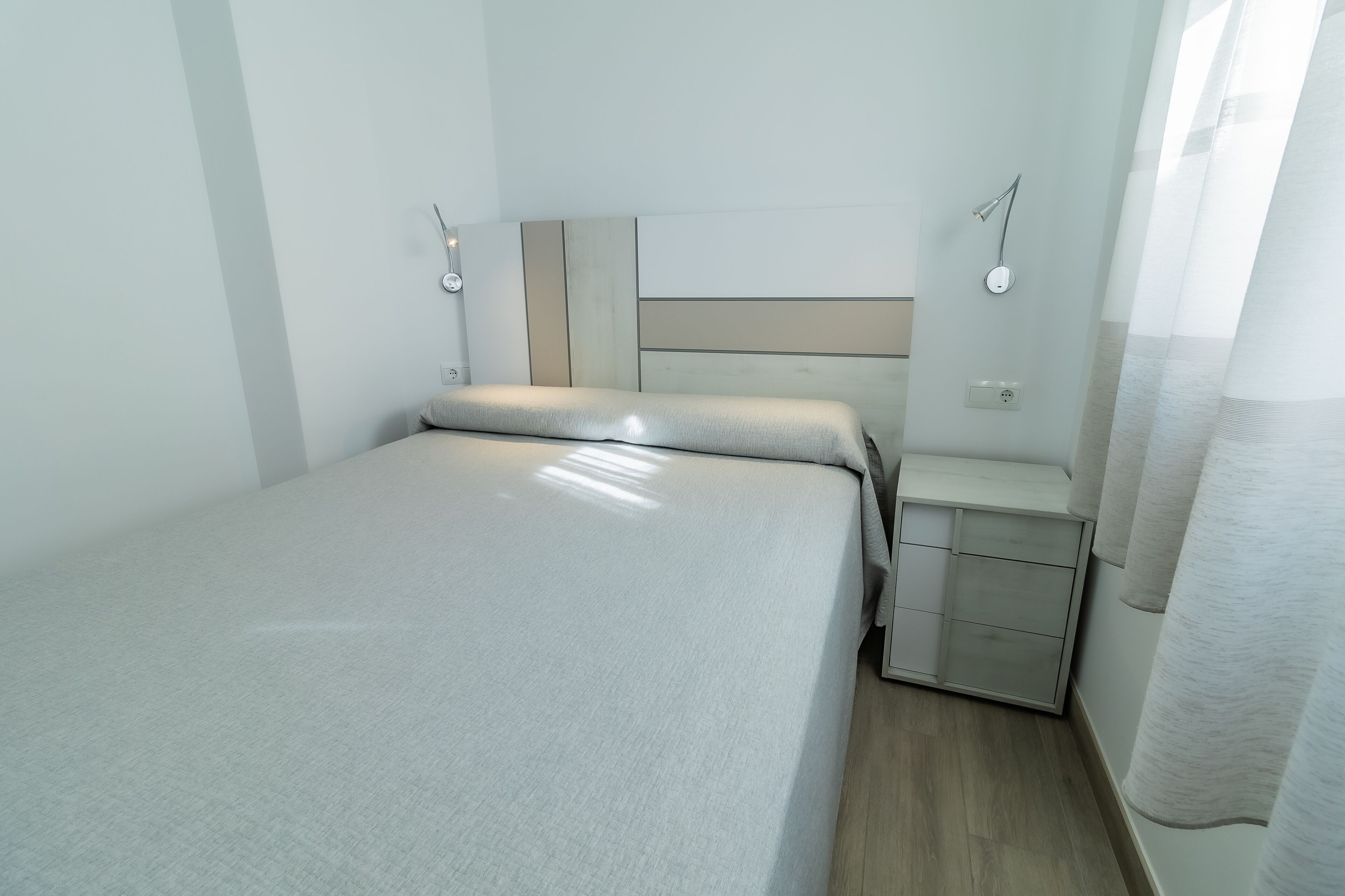 A small, neatly arranged bedroom with a bed, bedside tables, and a nightstand.