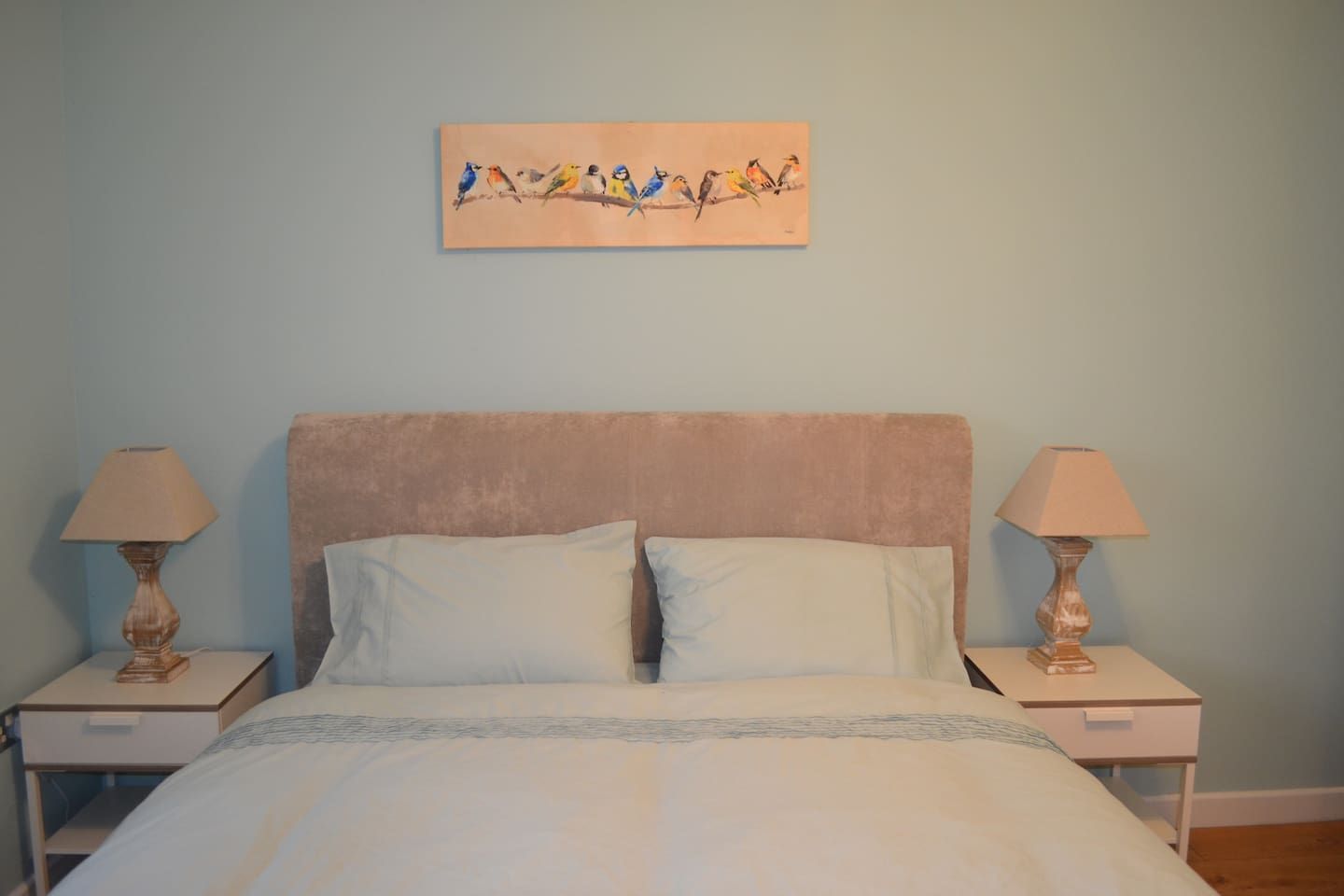 Een slaapkamer met een bed, twee nachtkastjes, twee lampen en een schilderij aan de muur.