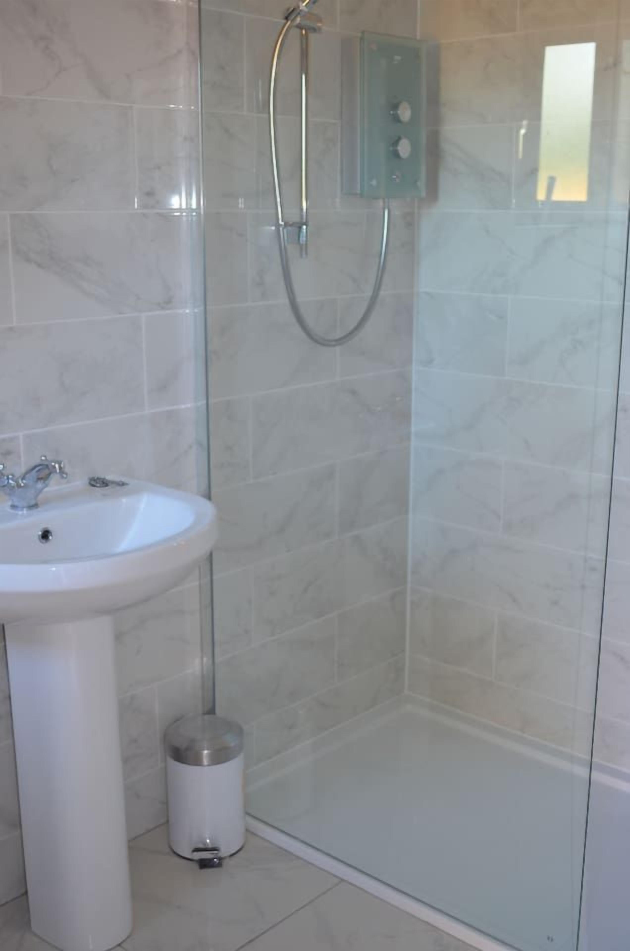 A bathroom with a glass-enclosed shower, a white sink, and a trash can.