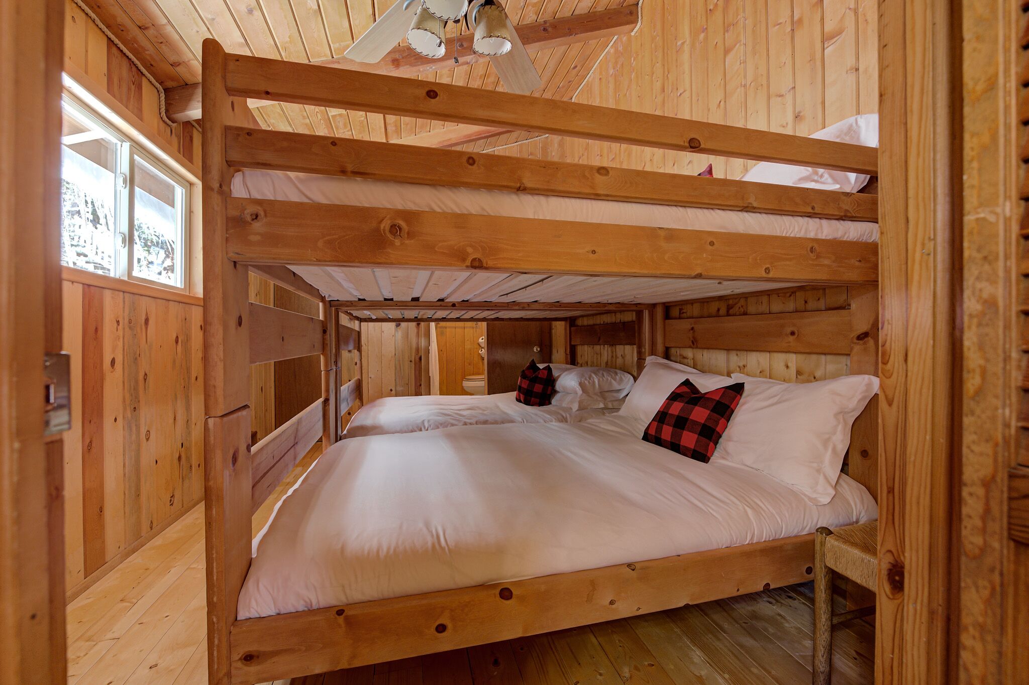 A wooden cabin room with bunk beds, a window with a view, and a wooden ceiling.