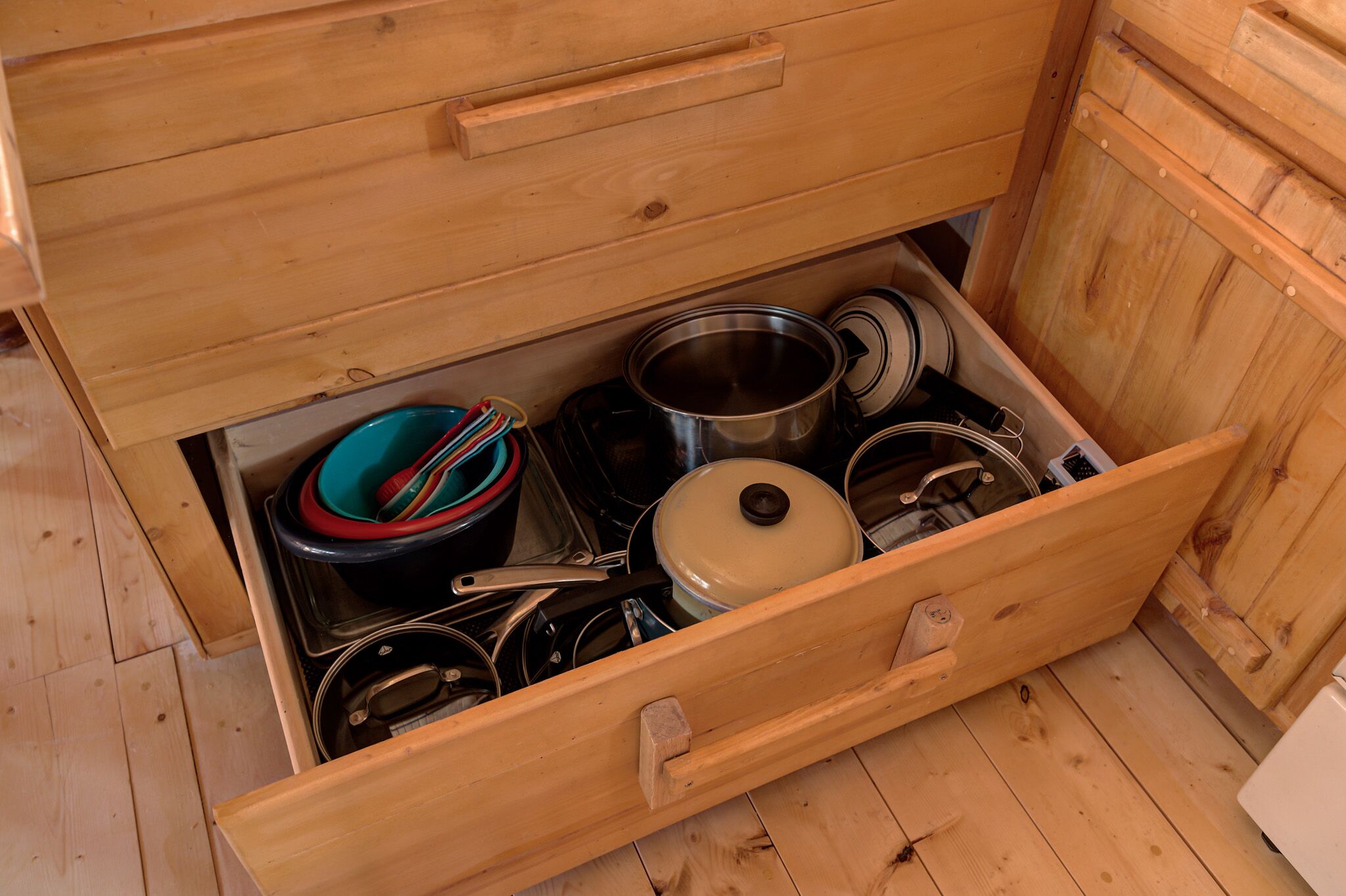 A wooden drawer with various kitchen utensils and cookware.