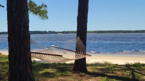 Un hamac tendu entre deux arbres, près d’une plage, d’où l’on a une vue dégagée sur l’eau et sur une jetée éloignée.
