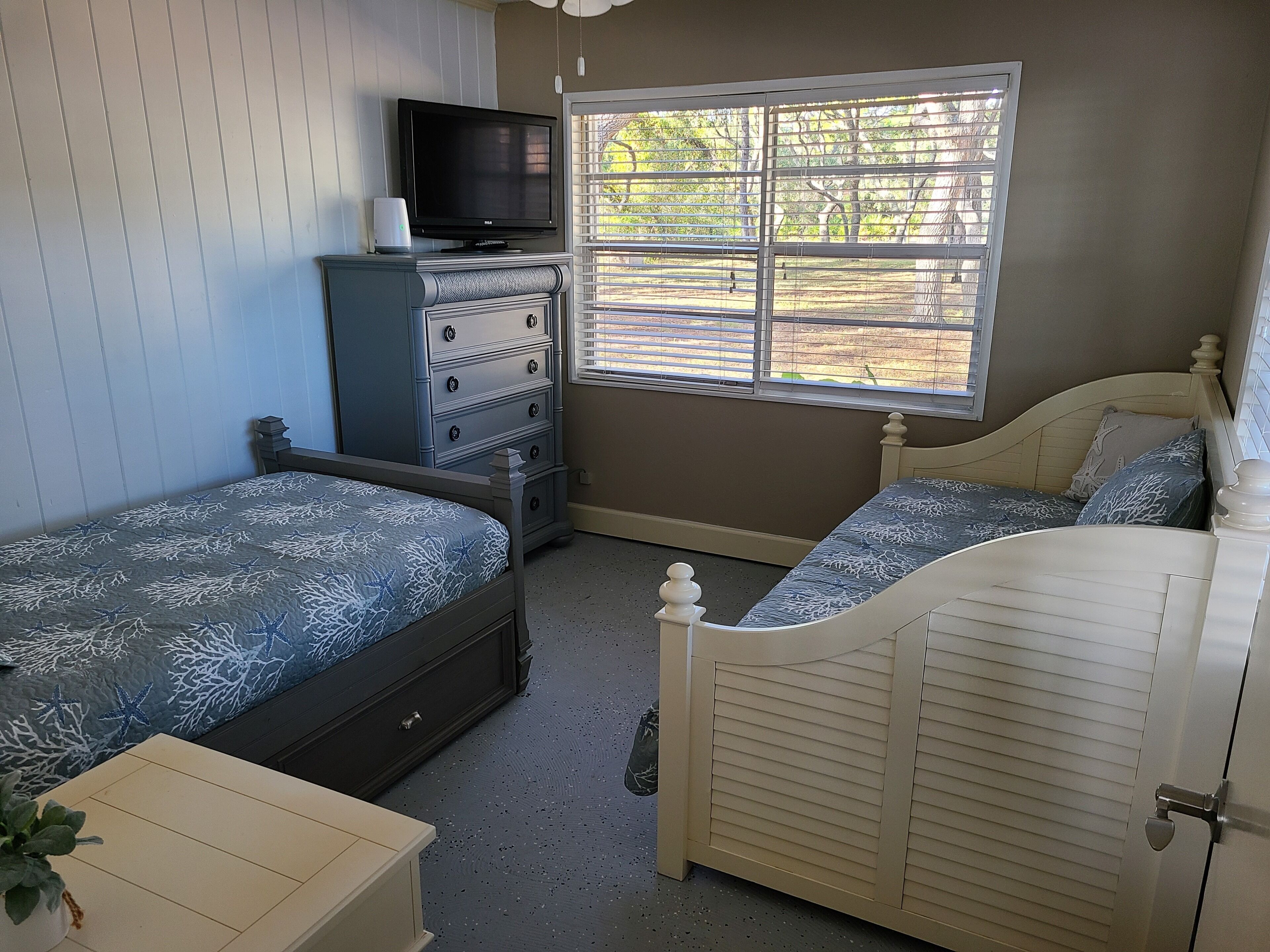Ein Schlafzimmer mit Bett, Kommode, Fernseher und Fenster.