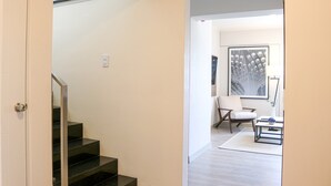A modern interior with a staircase, a white chair, a framed artwork, and a small table with a vase.