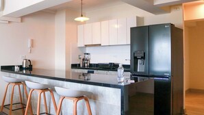 A modern kitchen with a large island, bar stools, a black refrigerator, and a coffee machine.