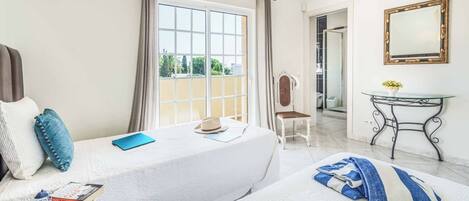 A hotel room with two beds, a desk, a chair, a mirror, and a view of the outside.