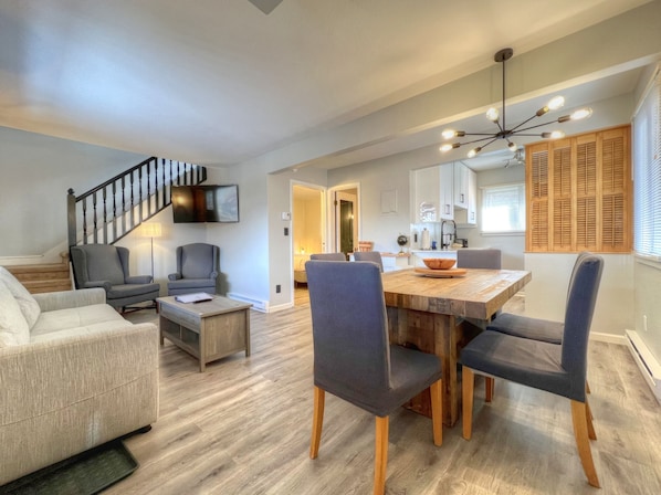 A modern living room with a staircase, a dining area with a wooden table and chairs, and a kitchen with white cabinets and wooden shutters. - Refreshed 2 Bedroom on the Shuttle Loop! (Mount Crested Butte)