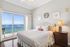 A bedroom with a large bed, a nightstand, and a view of the ocean through a sliding door.