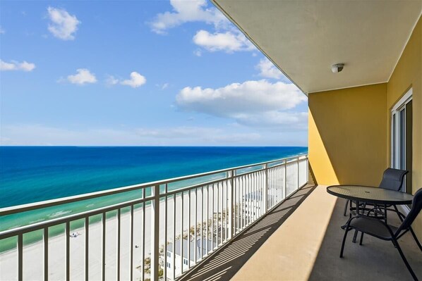 A balcony with a view of the ocean, a table with chairs, and a window.