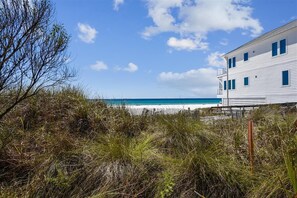A beachfront property with a white building, a wooden fence, and a clear view of the ocean.