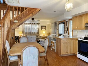 Un'accogliente cucina con mobili in legno, una zona pranzo con tavolo e sedie in legno, una scala con ringhiere in legno e una ventola a soffitto.