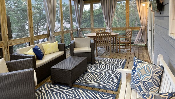 Un espacio de estar techado al aire libre con muebles de mimbre, una mesa y alfombras estampadas.