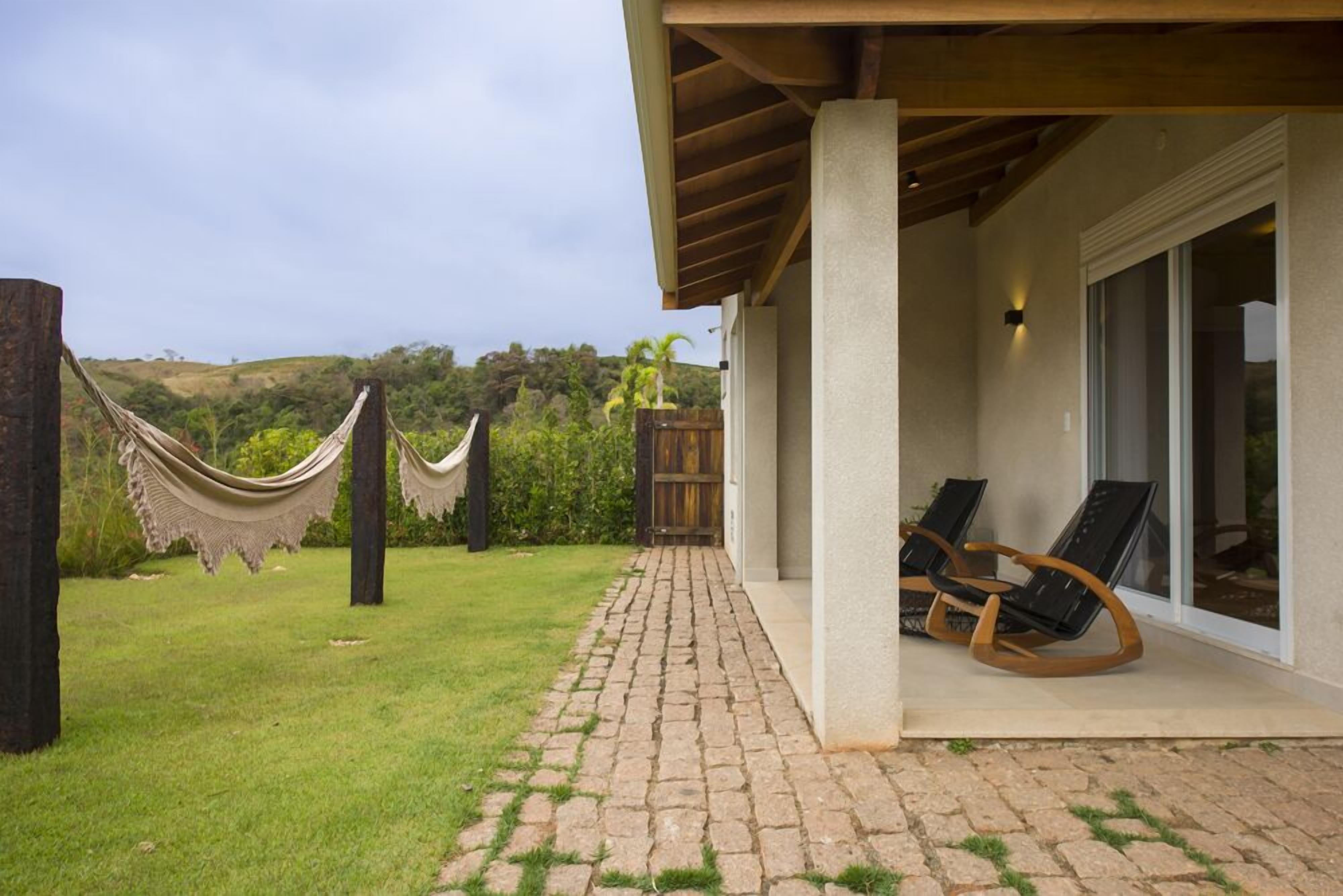 A covered outdoor area with a paved walkway, two rocking chairs, and a hammock.