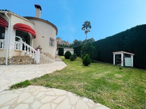 A house with a stone staircase leading to a white door, a red awning, and a small shed in the yard.