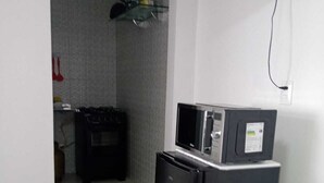 Une cuisine compacte équipée d’un réfrigérateur et d’un four à micro-ondes, d’une petite poubelle et d’une prise électrique visible sur le mur.